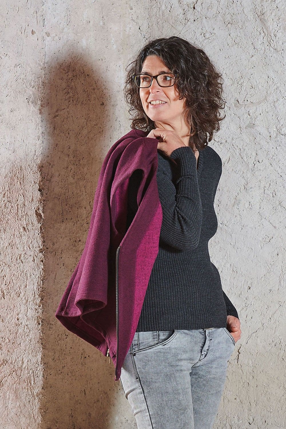 Frau trägt graues Rippshirt und hält brombeerfarbene Finkhof Weste Marlene über der Schulter