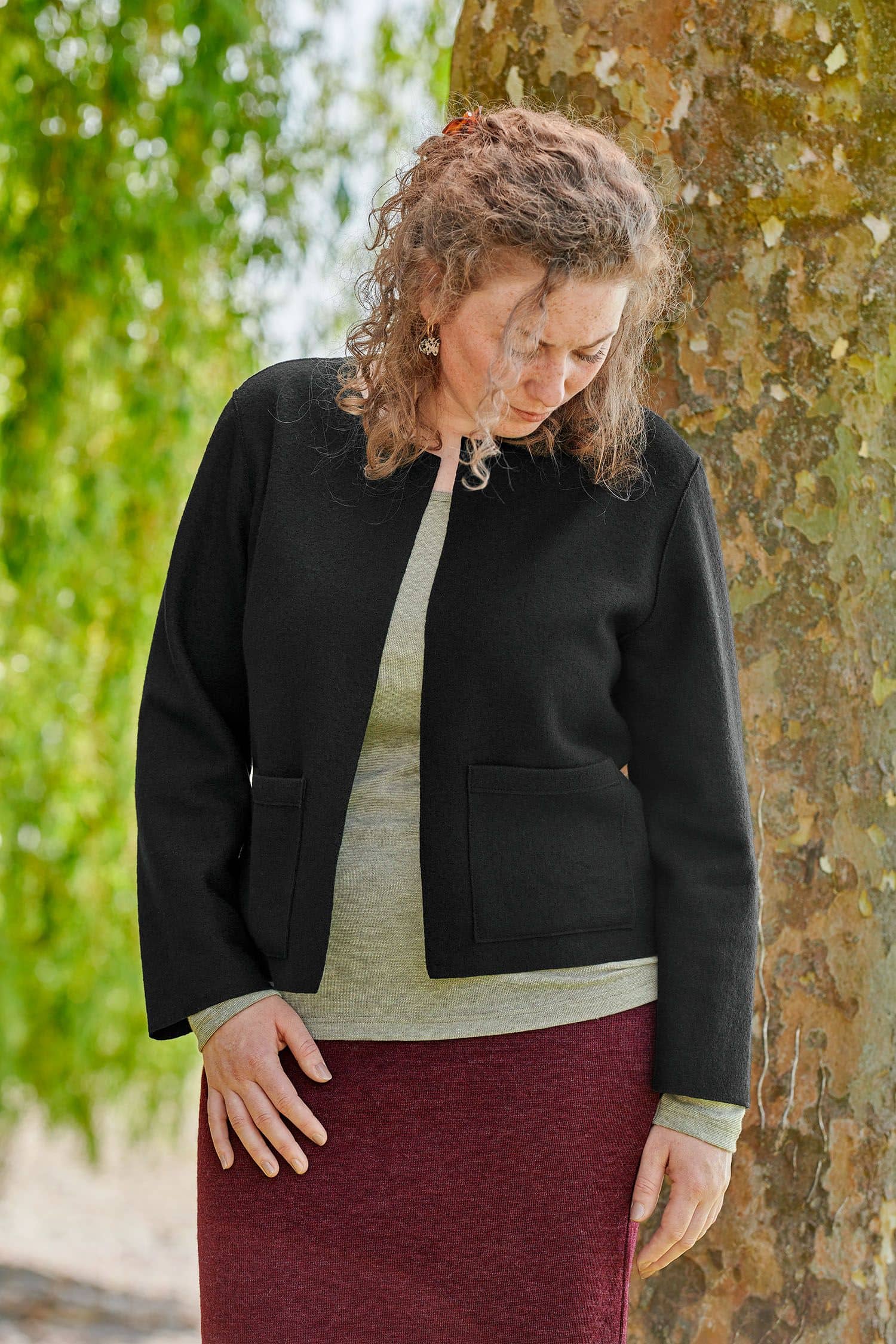 Frau trägt langen burgunderroten Strickrock, ein grünes Shirt und eine Jacke aus schwarzem Feinstrickstoff aus bio Wolle (kbT)
