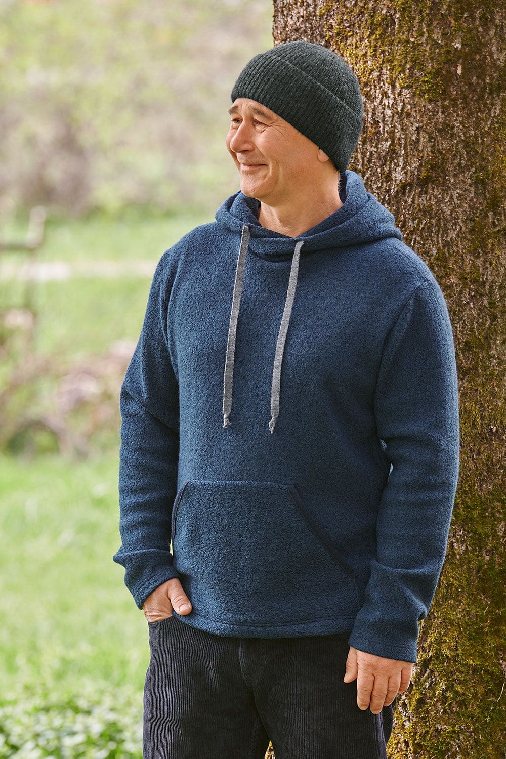 Herren-Hoody Mann steht vor Baum und trägt marineblauen Hoody aus bio Wolle (kbT) mit dunkelgrauer Mütze