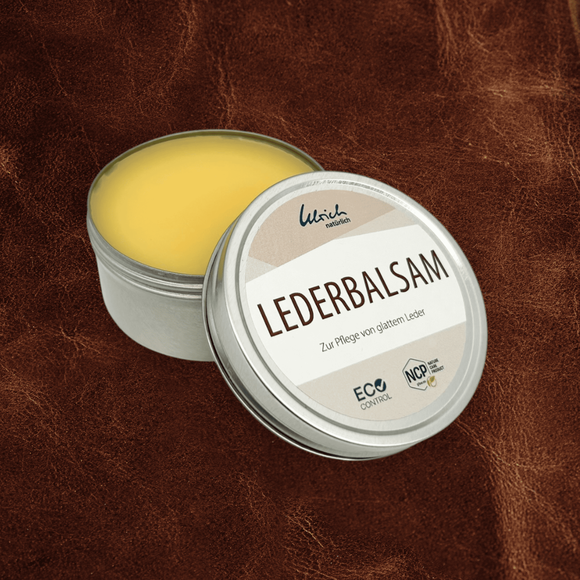 Lederbalsam aus Bienenwachs, Wollfett und Ölen in offener silberner Aludose auf braunem Leder