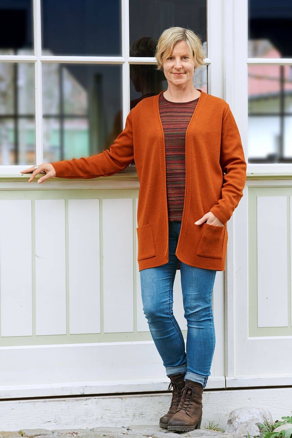 Frau mit gestreiftem Shirt und Jeans trägt orangen langen Cardigan aus bio Merinowolle (kbT)