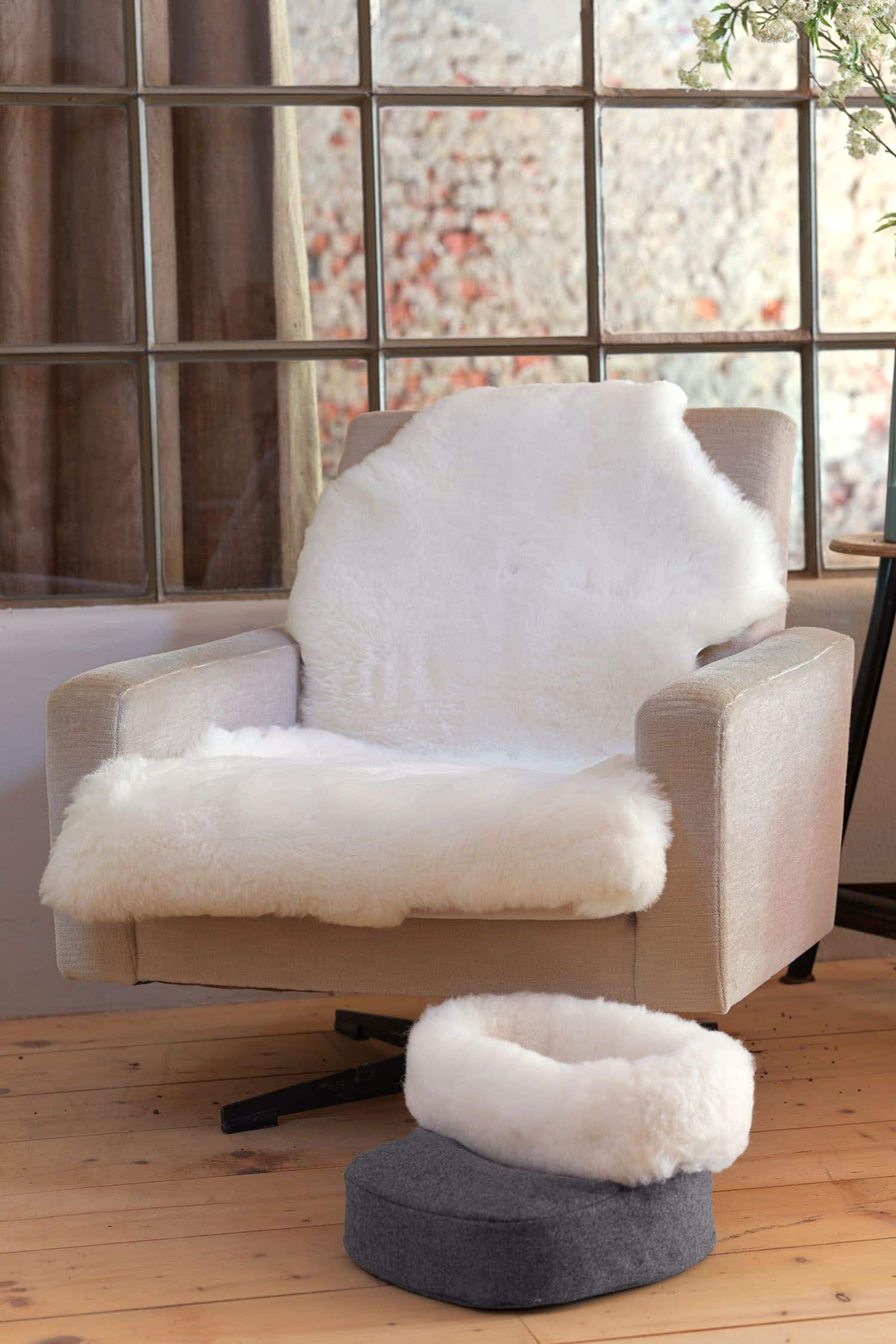 grauer Fußwärmer aus Schaffell und Schurwolle vom Finkhof steht vor einem Sessel