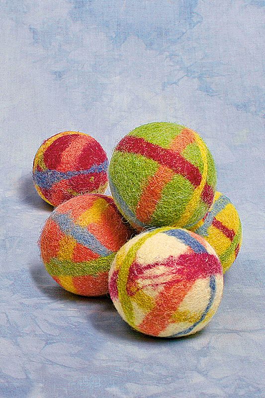 Filzball Wollbälle in verschiedenen Kombinationen aus bio Wolle (kbT) übereinander auf blauem Hintergrund