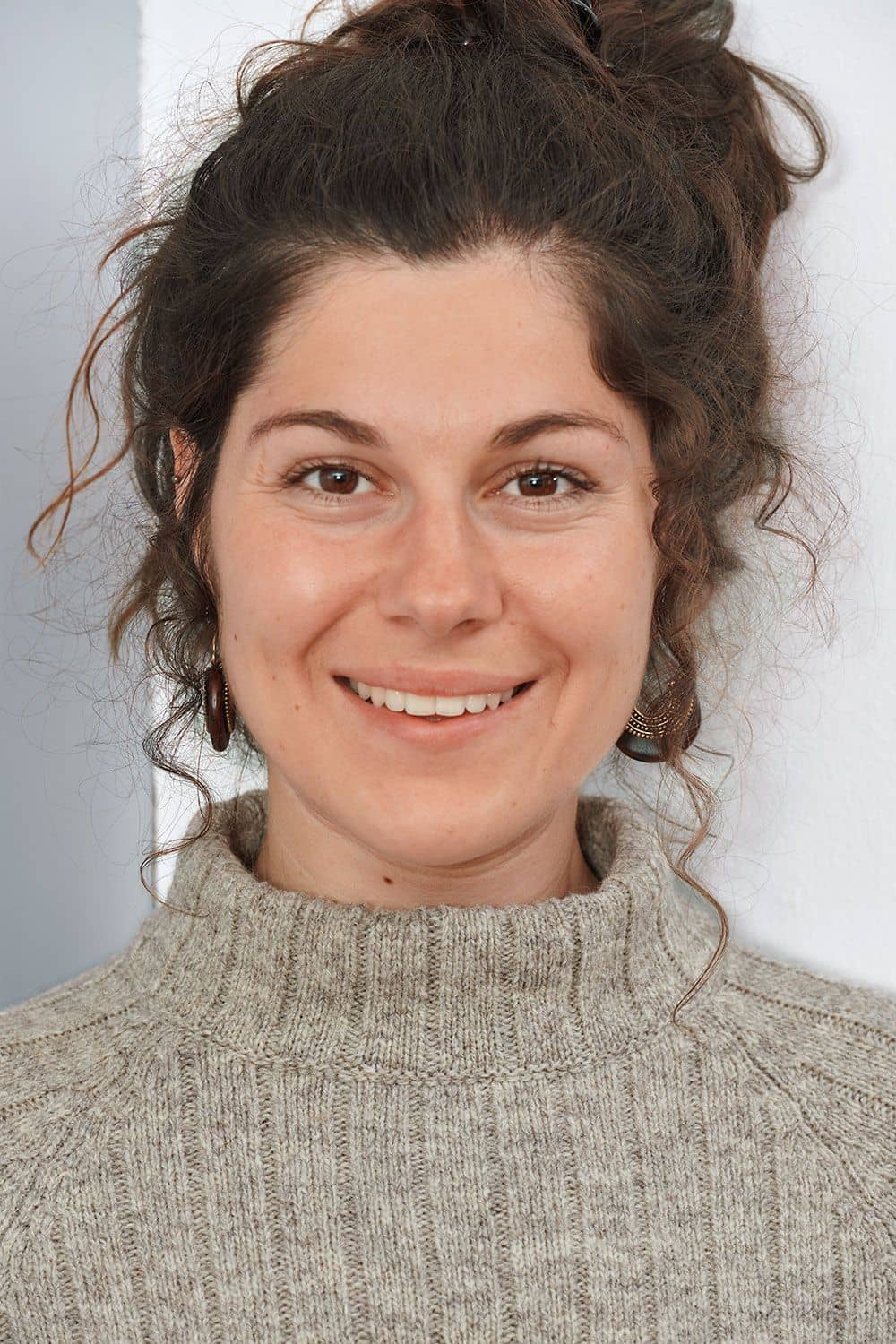 Portraitaufnahme von Frau mit dunklen Locken und grauem Finkhof Reglanpullover aus bio Wolle (kbT)