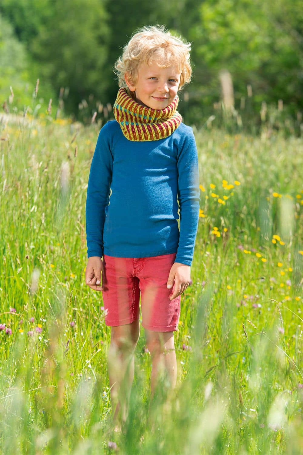 Kind mit blauem Shirt auf Wiese trägt bunt gestrickten Loopschal