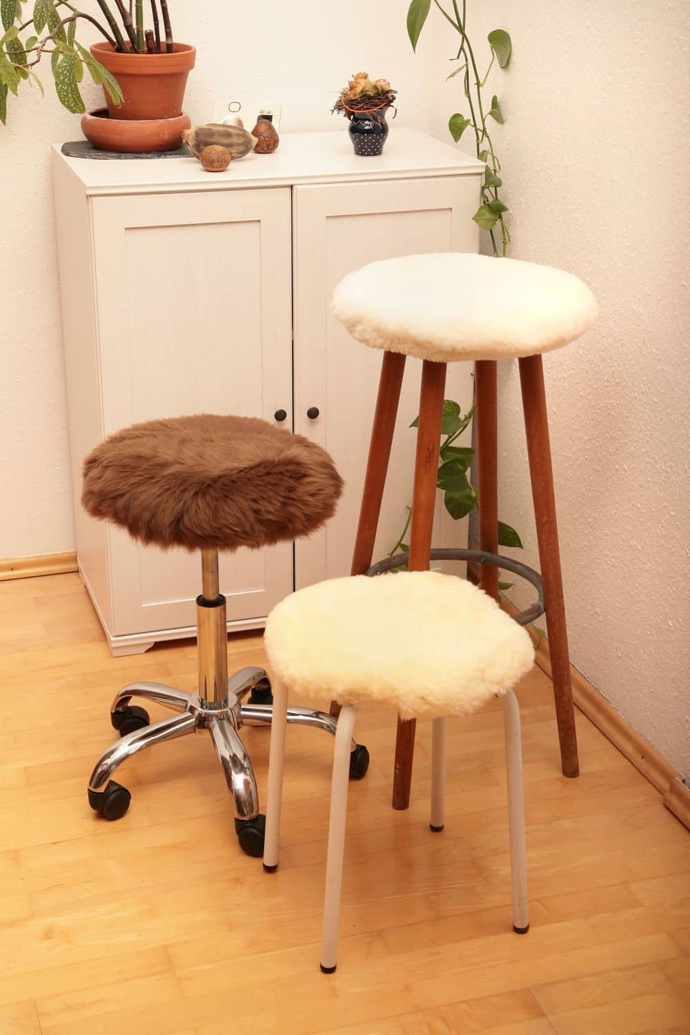 Hockerbezug Finkhof Hockerbezüge aus Schaffell relugan gegerbt auf verschiedenen Stühlen in braun, weiß und gelblich vor Kommode