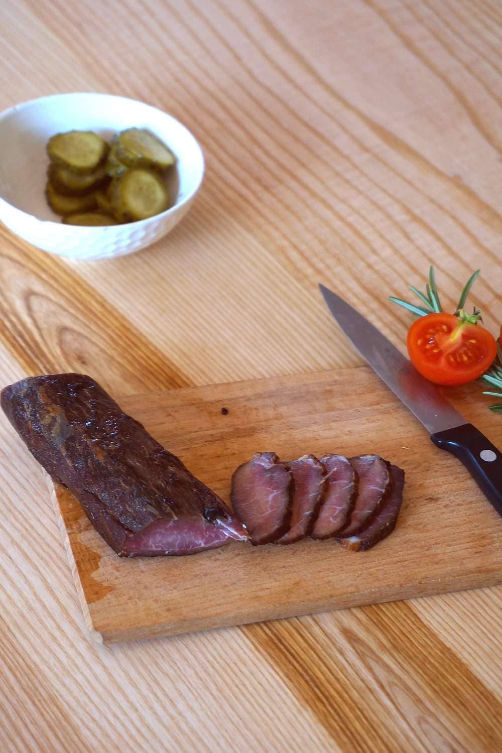 Bio-Lende vom Schaf aufgeschnittenes Rauchfleisch aus bio Lende vom Schaf vom Finkhof auf Holzbrett mit Tomaten und Essiggurken