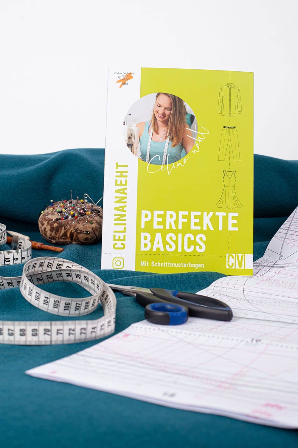 Celina näht perfekte Basics Buch ,,Perfekte Basics" von Celinanäht auf blauem Stoff mit Schnittmuster und Nähutensilien