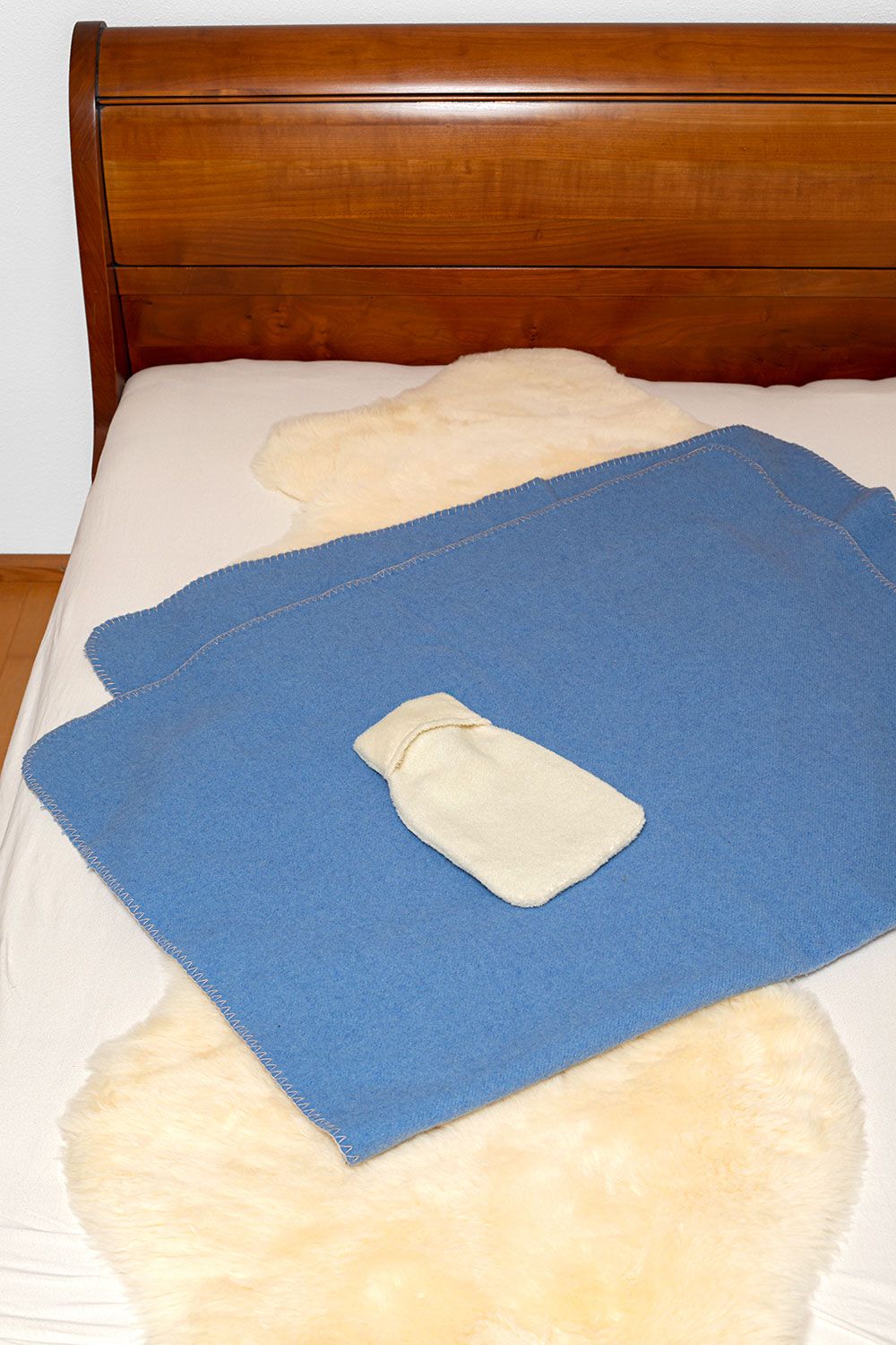 Wärmflaschenbezug Lammflor naturweiß klein naturweißer Wärmflaschenbezug aus Lammflor mit bio Baumwolle (kbA) vom Finkhof liegt auf blauem Teppich in Bett