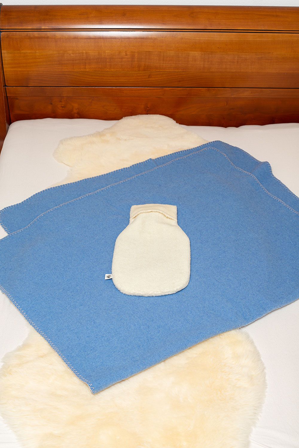 Wärmflaschenbezug Lammflor naturweiß groß naturweißer Wärmflaschenbezug aus Lammflor mit bio Baumwolle (kbA) vom Finkhof liegt auf blauem Teppich in Bett