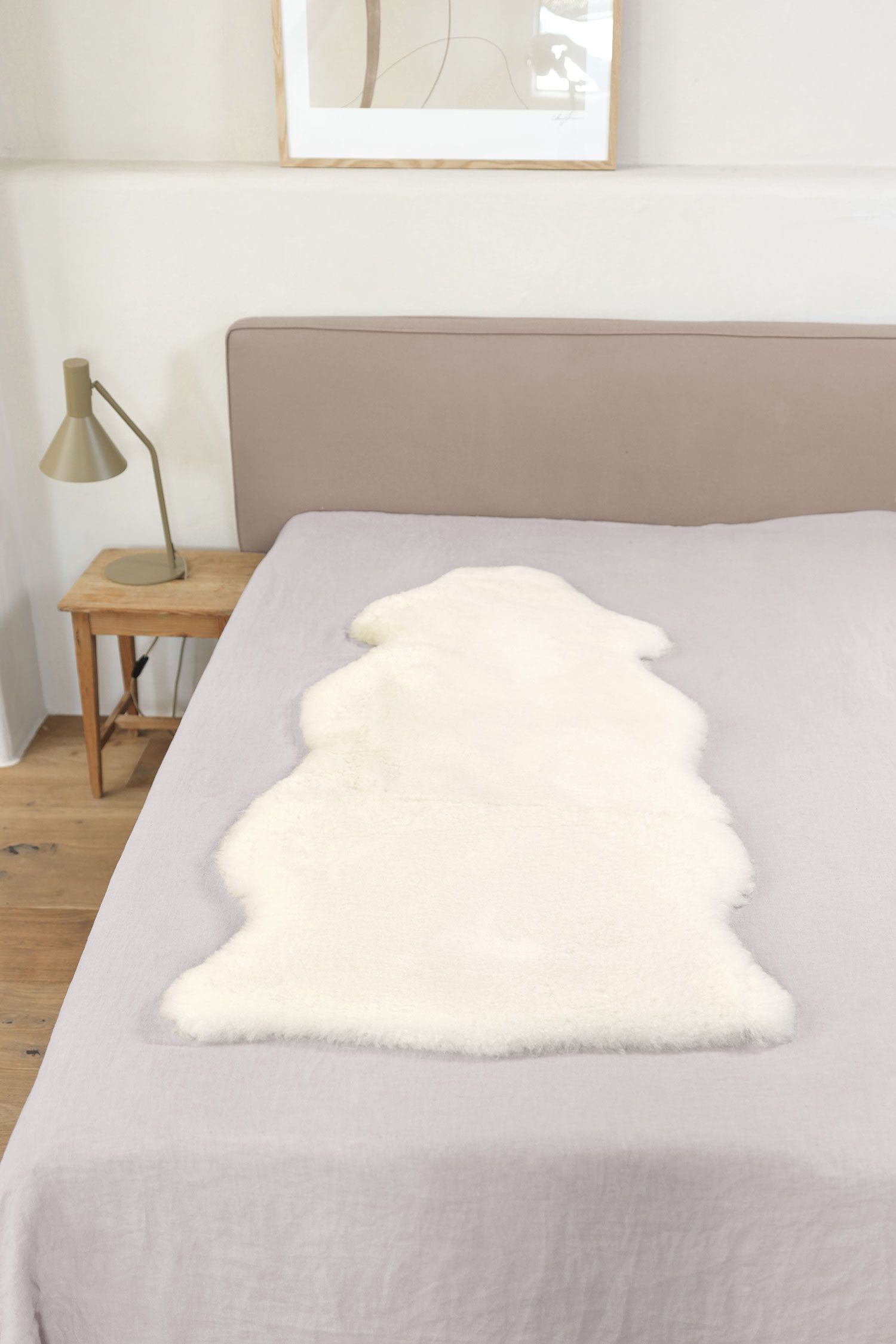 weiße pflanzlich gegerbte Felldecke in natürlicher Form aus Schaffell vom Finkhof auf grauem Bett