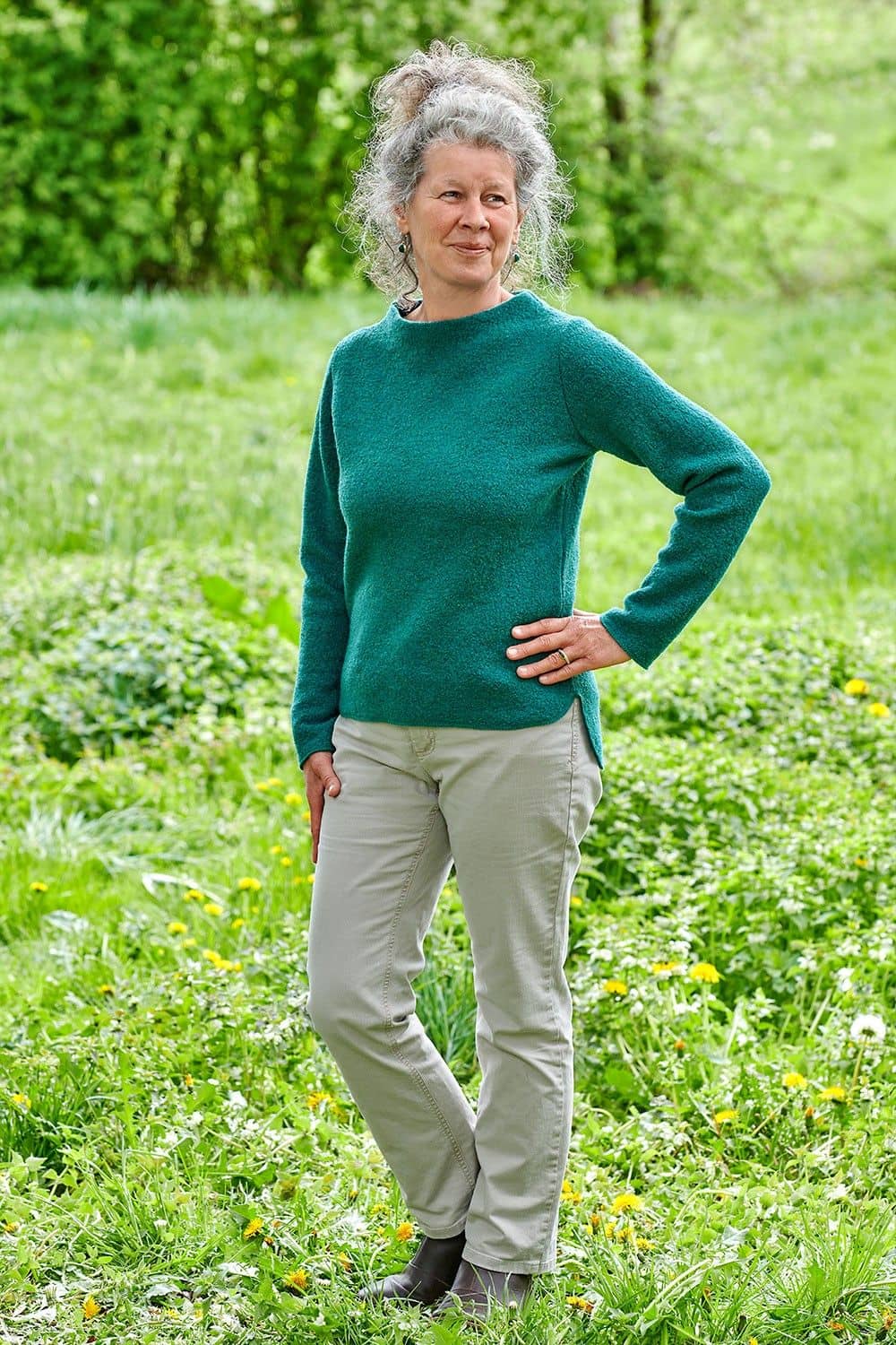 Frau steht in der Natur und trägt türkisen Pulli aus bio Wolle (kbT)