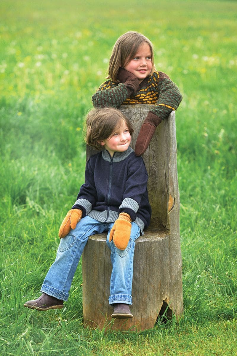 Fellhandschuhe für Kinder Kind sitzt auf Baumstumpf, Anderes steht dahinter beide tragen Fellhandschuhe aus Schaffell und Pelzvelour