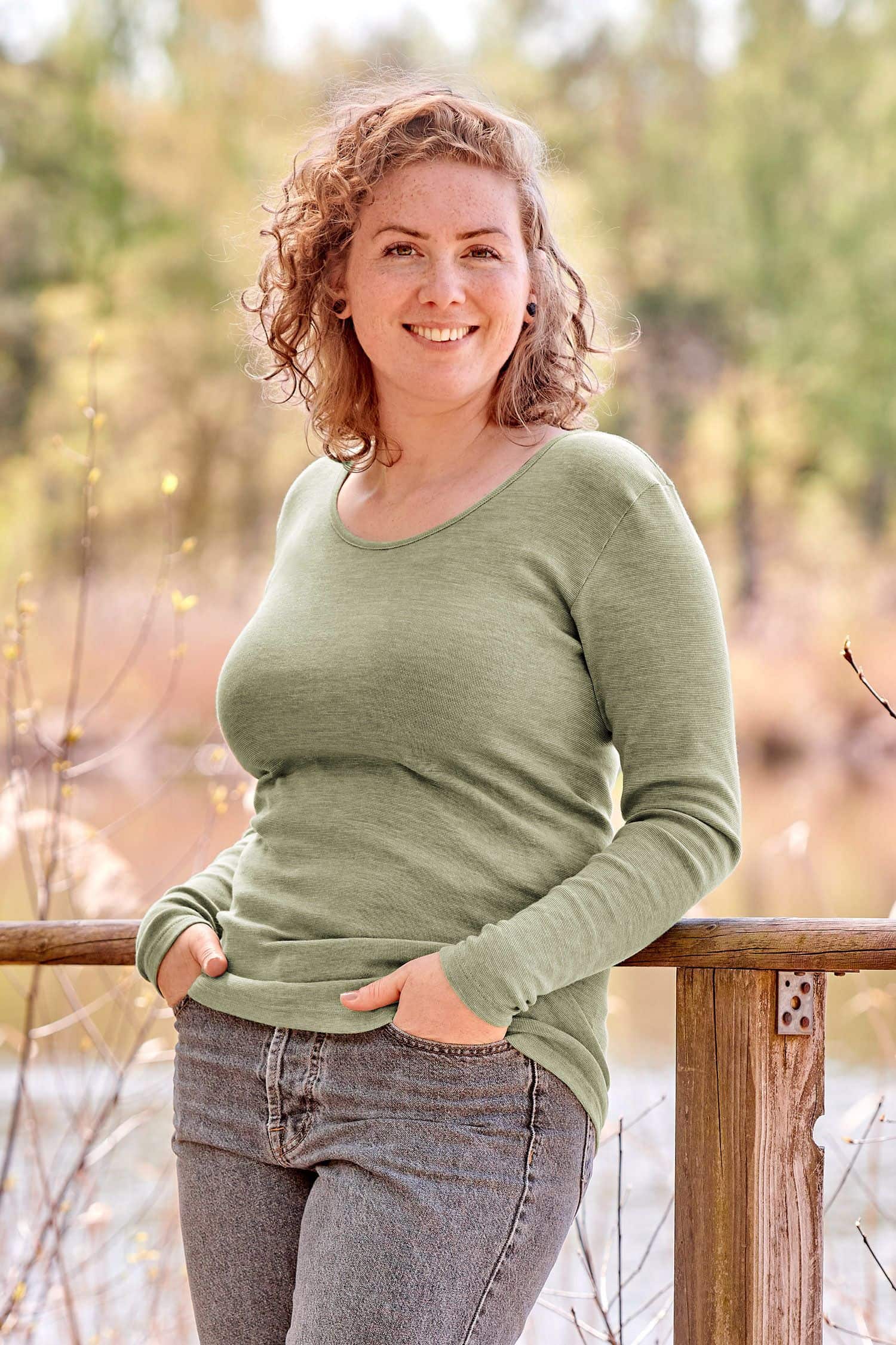 Frau lehnt an Geländer und trägt grünes Langarmshirt aus bio Wolle (kbT), bio Baumwolle (kbA) und Seide