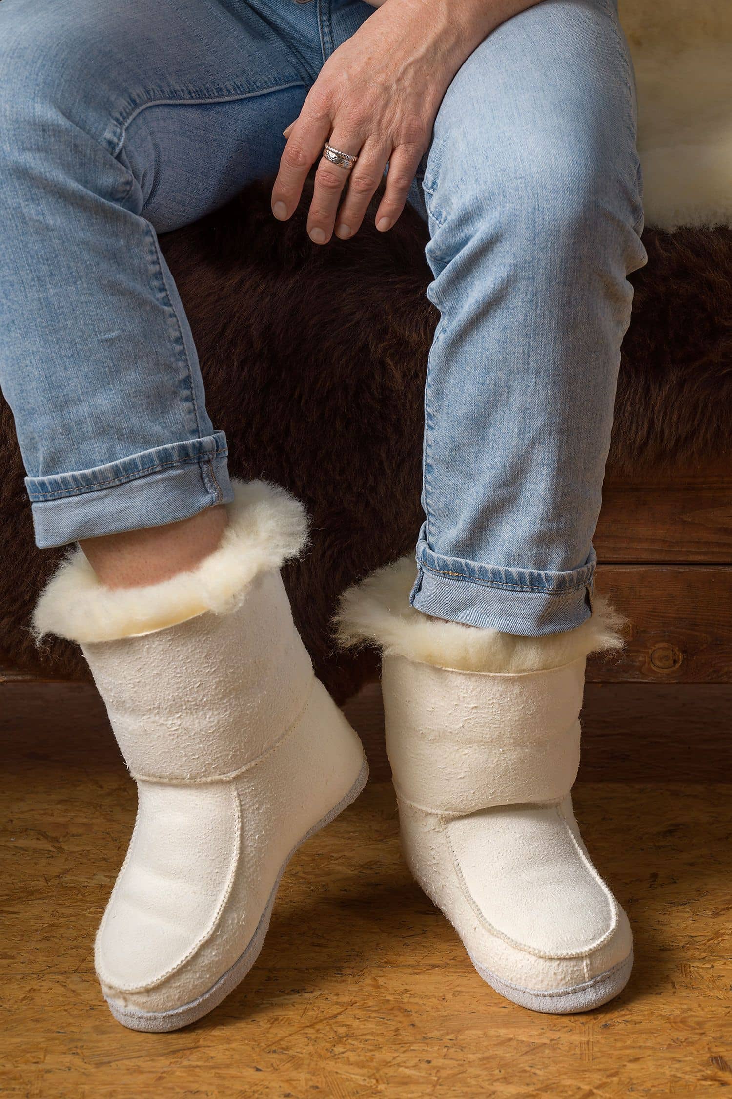 Person trägt relugan gegerbte Fellschuhe aus Schaffell und Rindsleder vom Finbkhof und sitzt auf einer Bank mit Fell