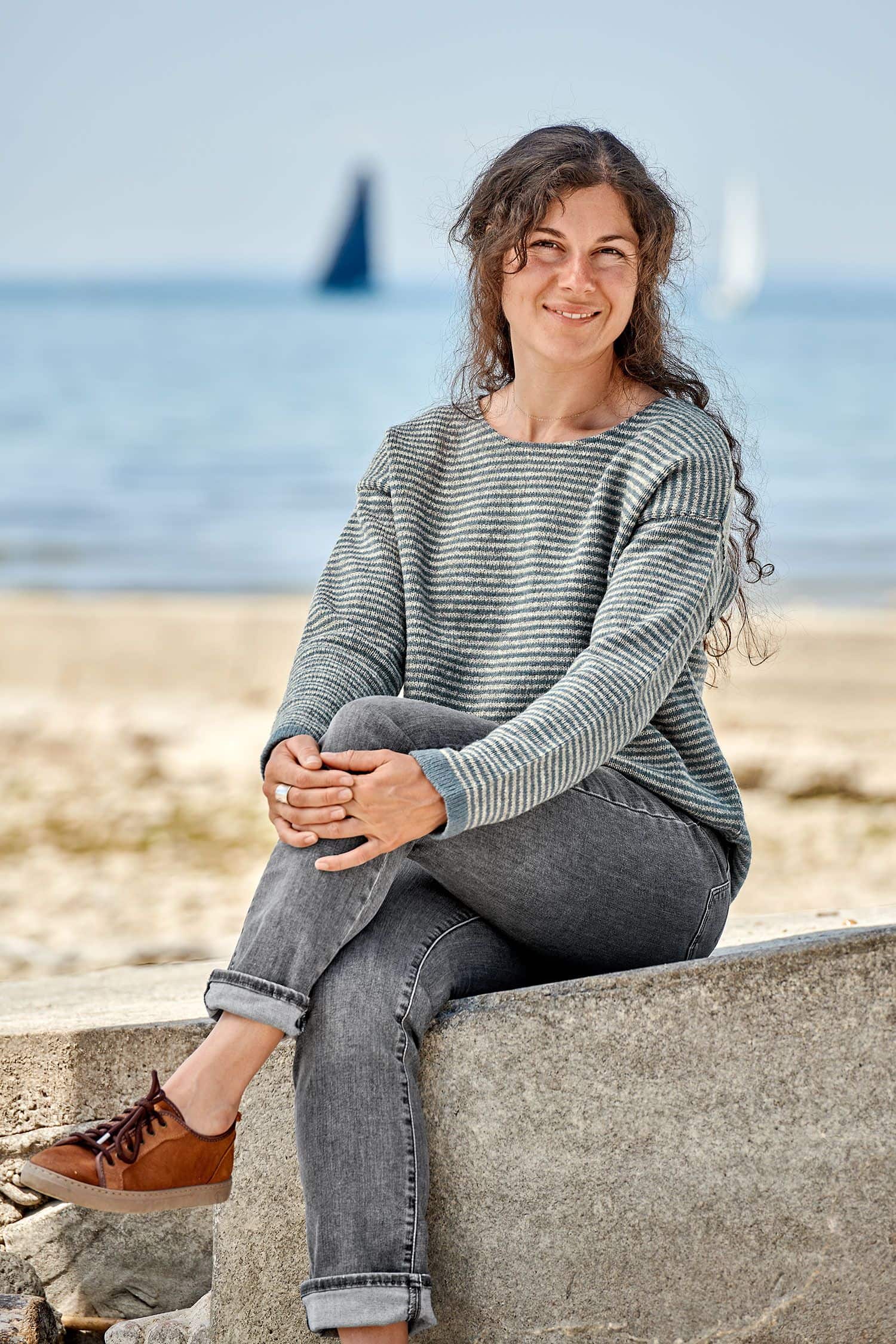 Finkhof-Damen-Ringelpulli blau/grau Gr. M Frau sitzt auf Stein und trägt einen grau blauen Ringelpulli vom Finkhof aus bio Merinowolle (kbT)