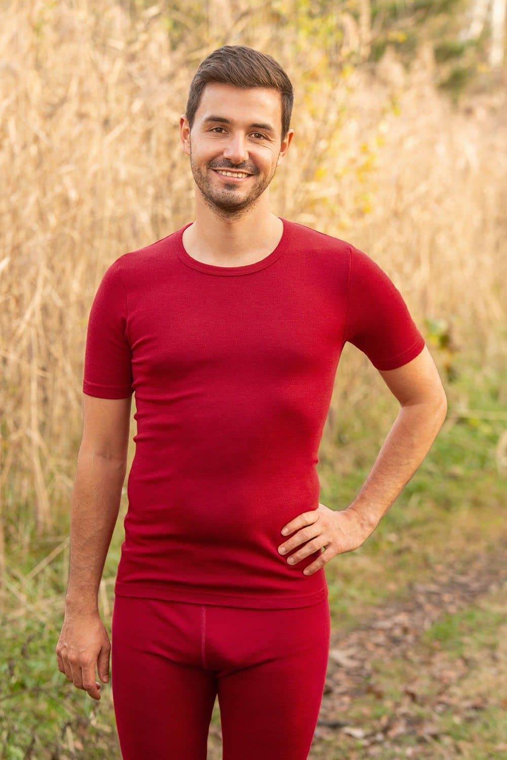 Mann trägt rotes Kurzarmshirt aus bio Wolle (kbT) und eine rote lange Unterhose, verschwommener Hintergrund
