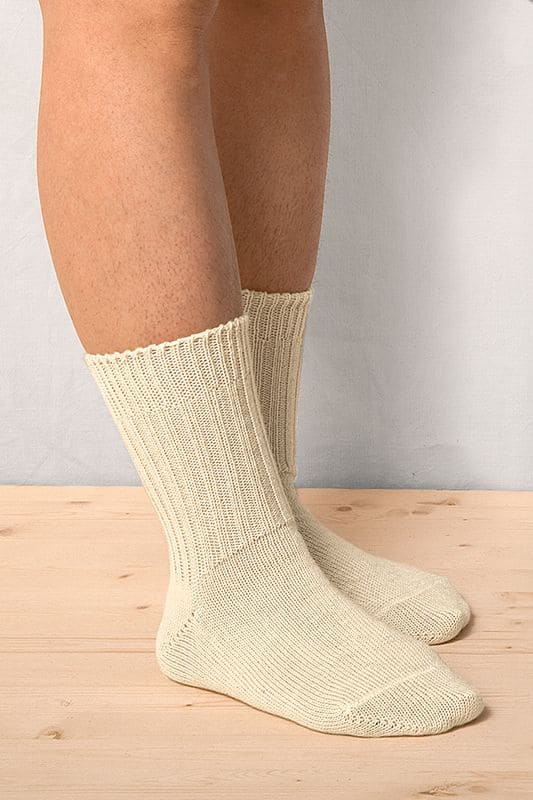 Person steht auf Holzboden und trägt naturweiße Wollsocken aus bio Wolle (kbT) in mittlerer Dicke