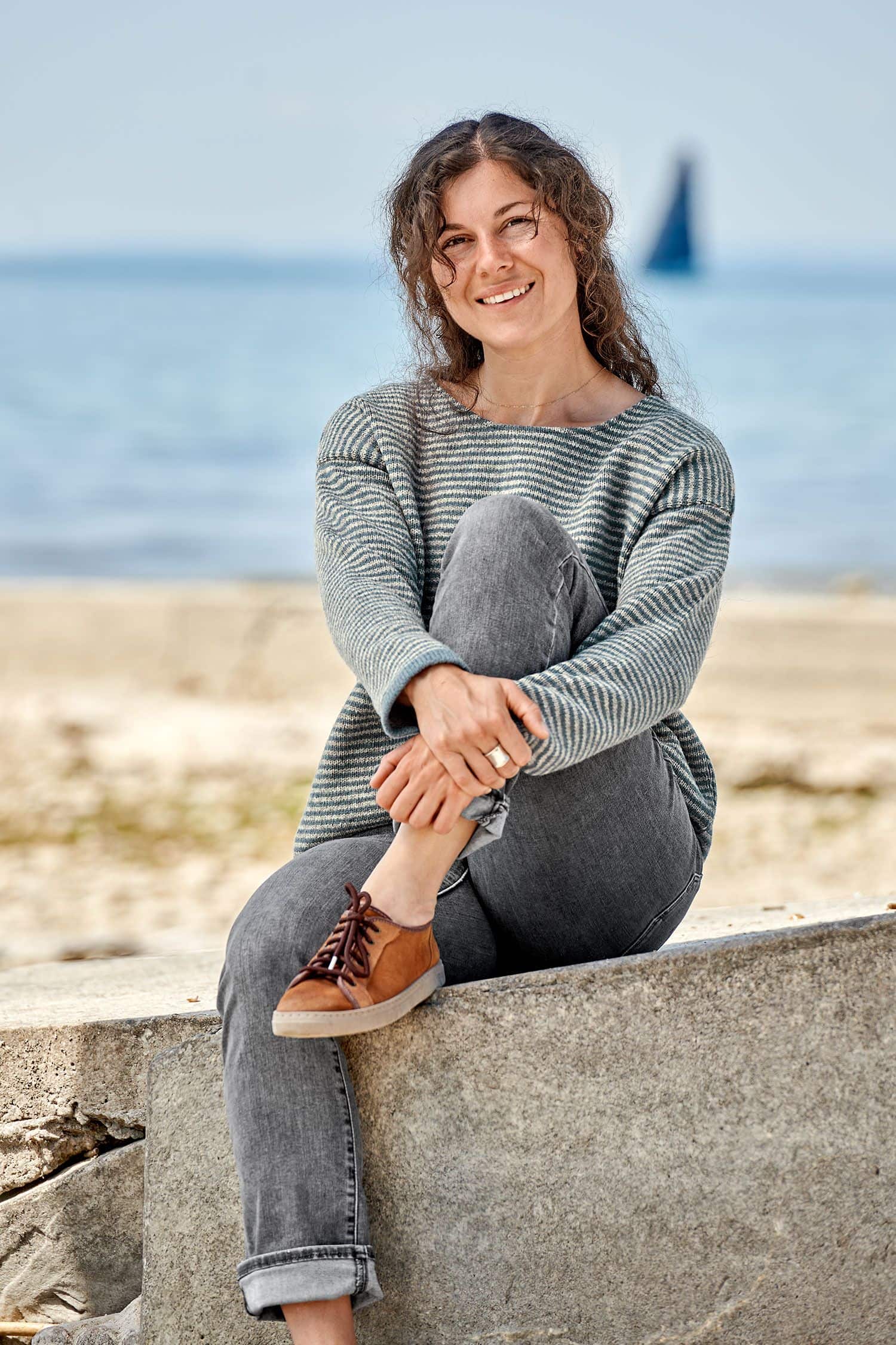 Frau sitzt auf Stein und trägt einen grau blauen Ringelpulli vom Finkhof aus bio Merinowolle (kbT)
