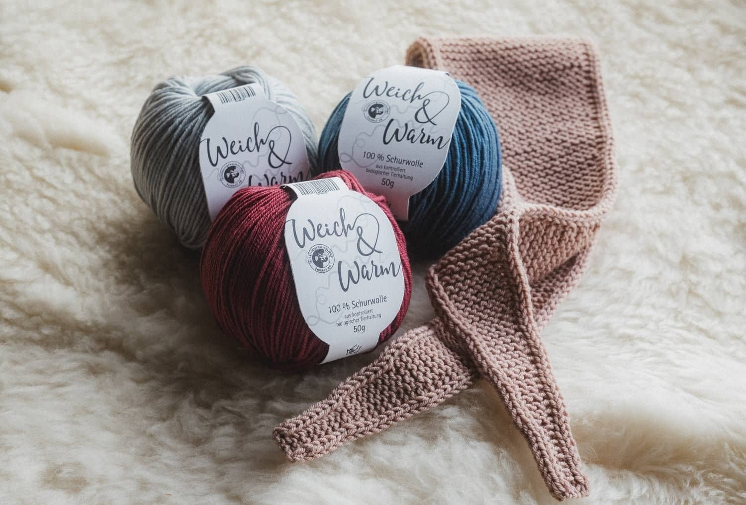 rosafarbener Mini-Schal liegt mit der Finkhof Weich&Warm Wolle auf einem weißen Fell