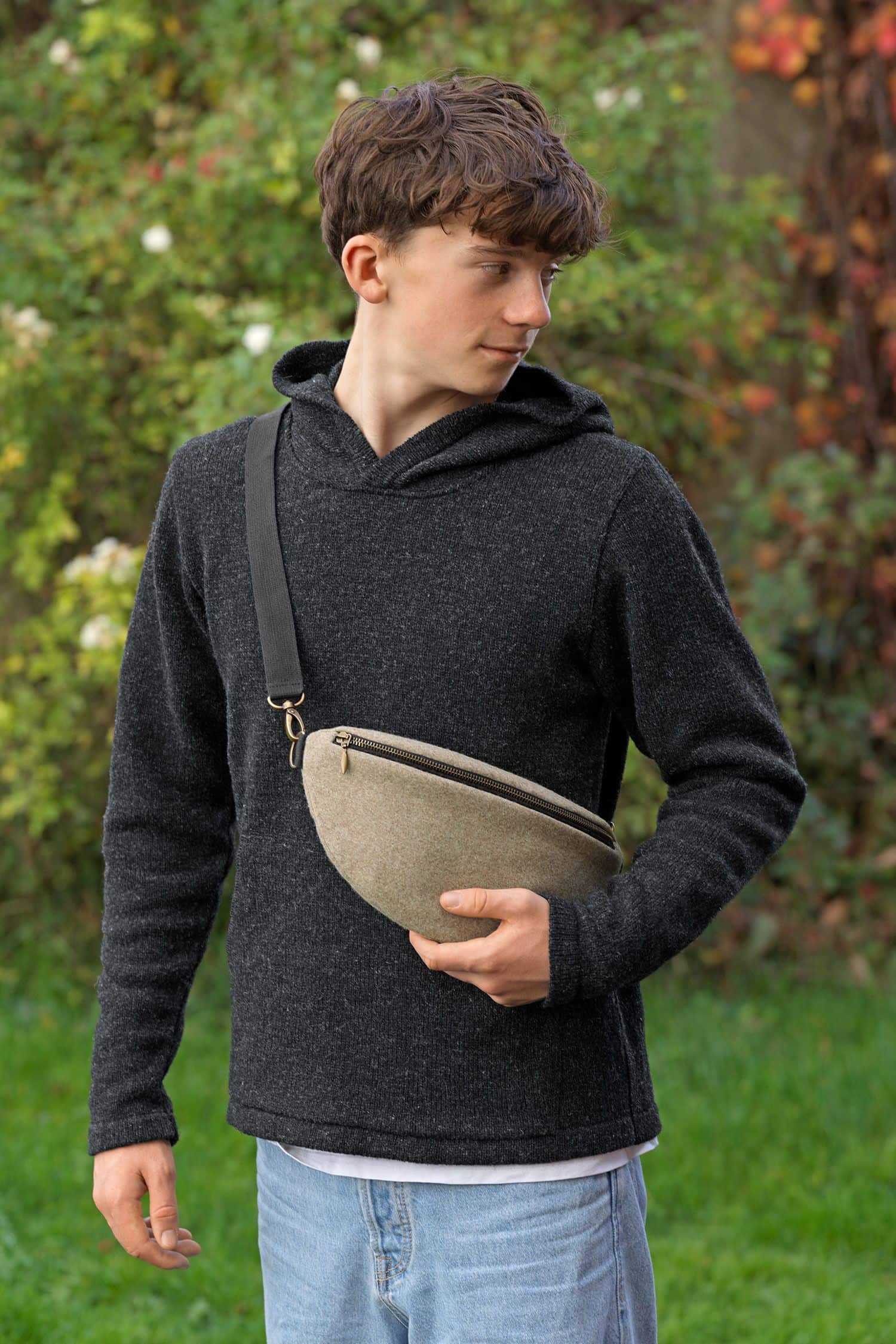 Junge trägt dunkelgrauen Kapuzenpulli und beige Bauchtasche aus Loden (Webstoff aus Schurwolle) vom Finkhof