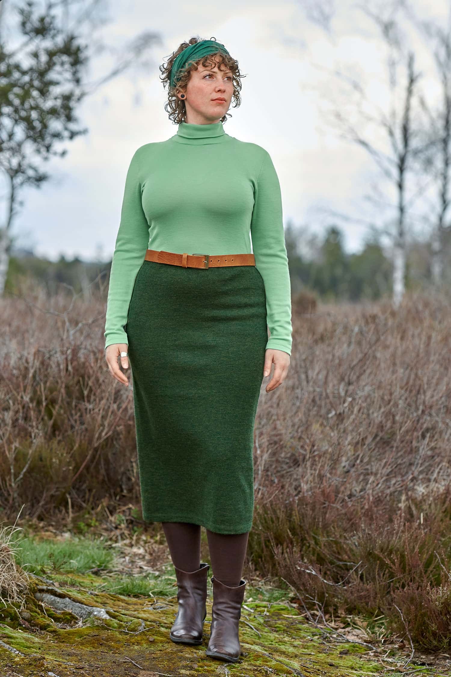 Frau trägt langen grünen Strickrock aus bio Wolle (kbT) mit grünem Langarmshirt und braunen Accessoires