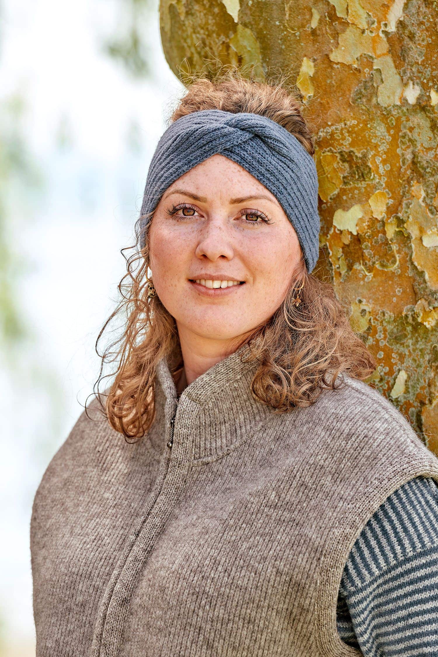 Finkhof-Stirnband Twist gefärbt rauchblau Frau trägt braune Weste und rauchblaues Stirnband mit Twist aus bio Wolle (kbT) vom Finkhof