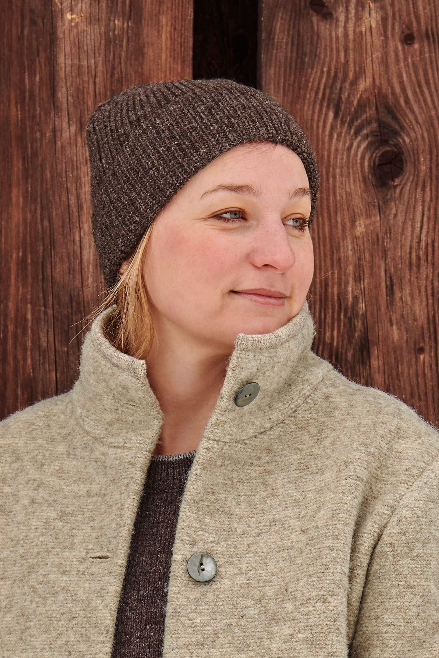 Frau trägt eine braune Finkhof Mütze aus bio Wolle (kbT) und einen Wollwalkmantel vom Finkhof