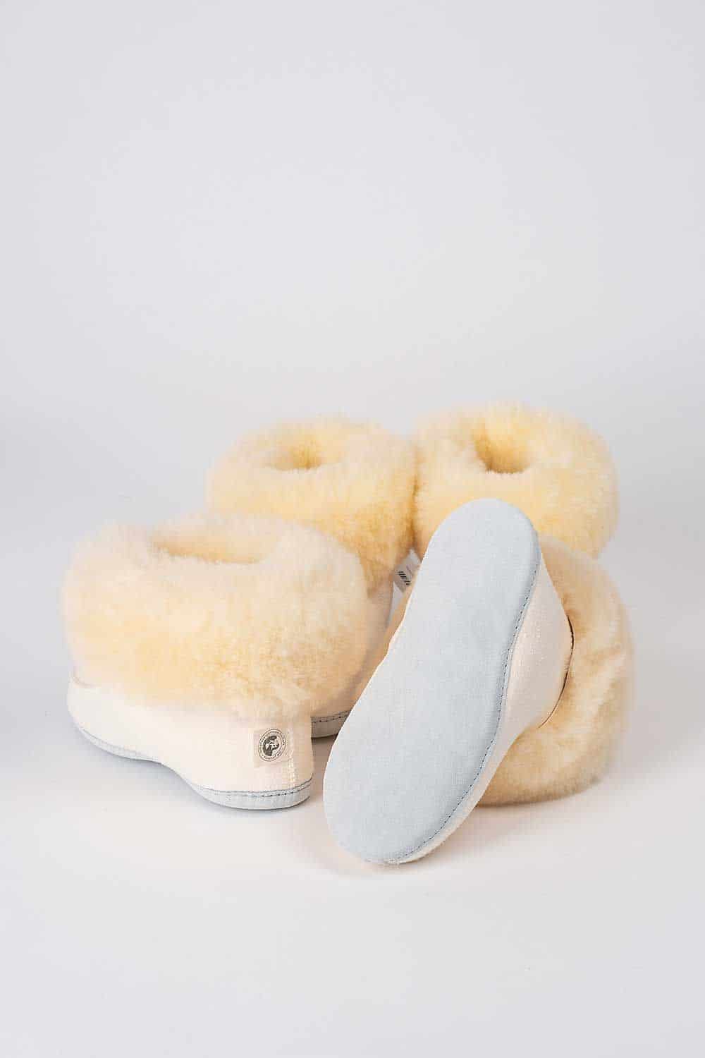 Drei weiße Finkhof-Fellschuhe von hinten, einer davor mit sichtbarer Sohle – aus Relugan-Schaffell und Rindsleder