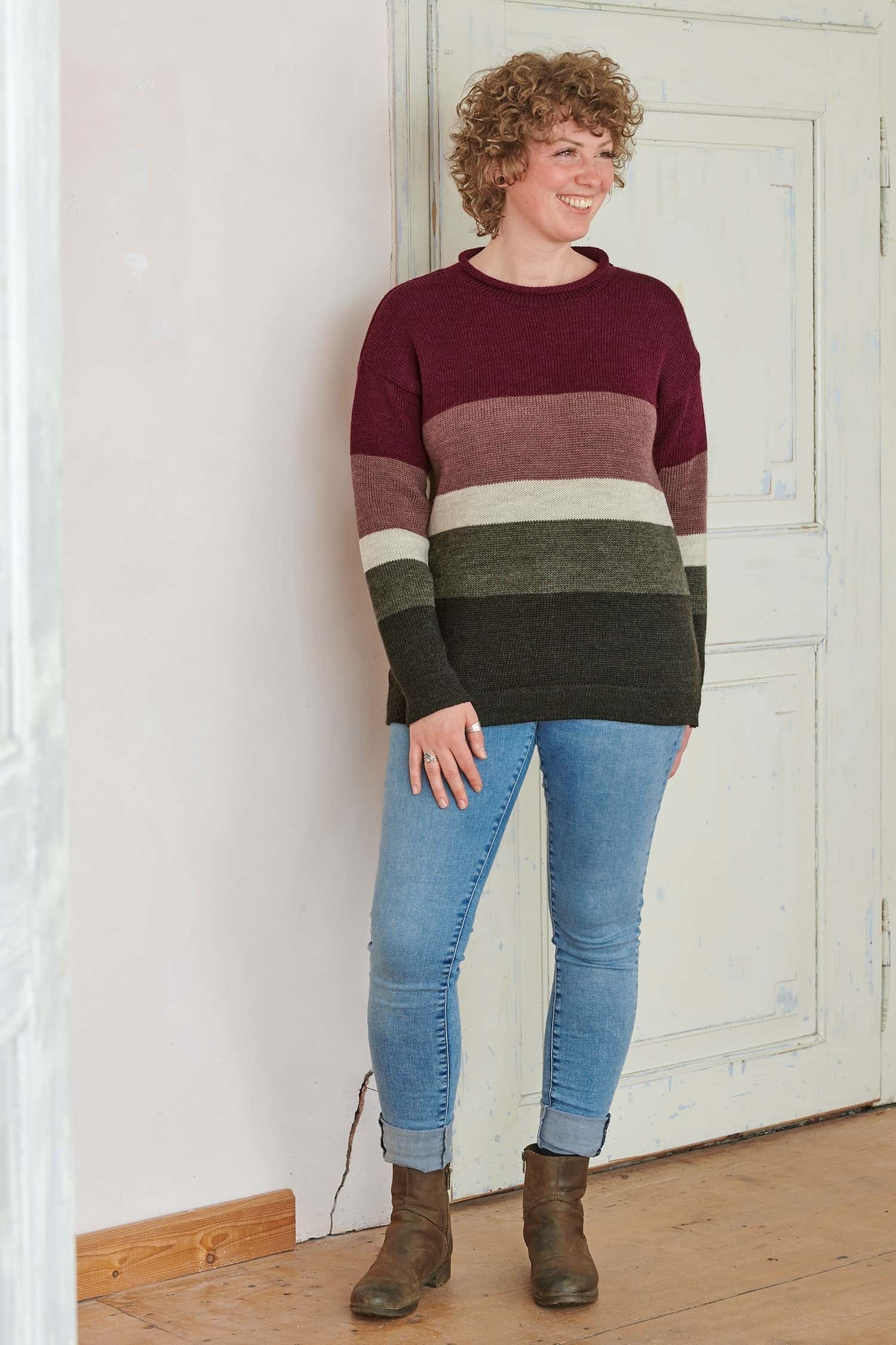 lachende Frau trägt Jeans und Pullover mit rot grünen Blockstreifen aus bio Wolle (kbT)