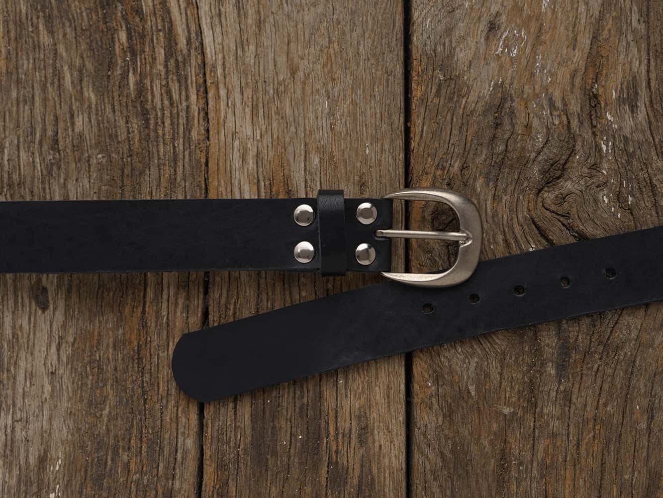 schwarzer Damengürtel aus Rindsleder mit einer silberfarbenen Schnalle auf einem Holzboden