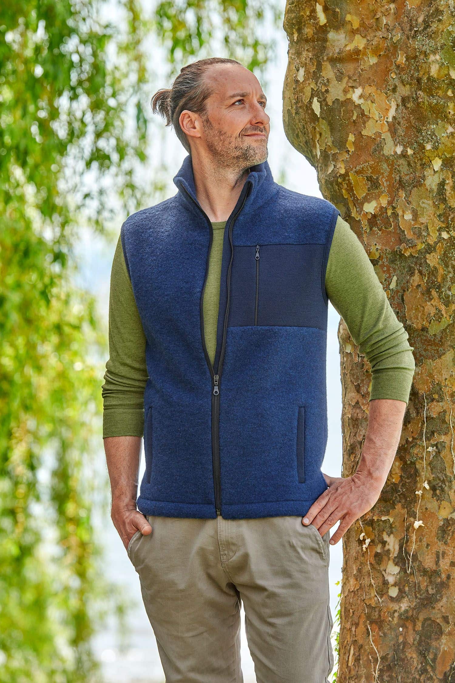 Mann trägt ein grünes Langarmshirt und eine marineblaue Wollfleece Weste aus bio Merinowolle (kbT) vom Finkhof