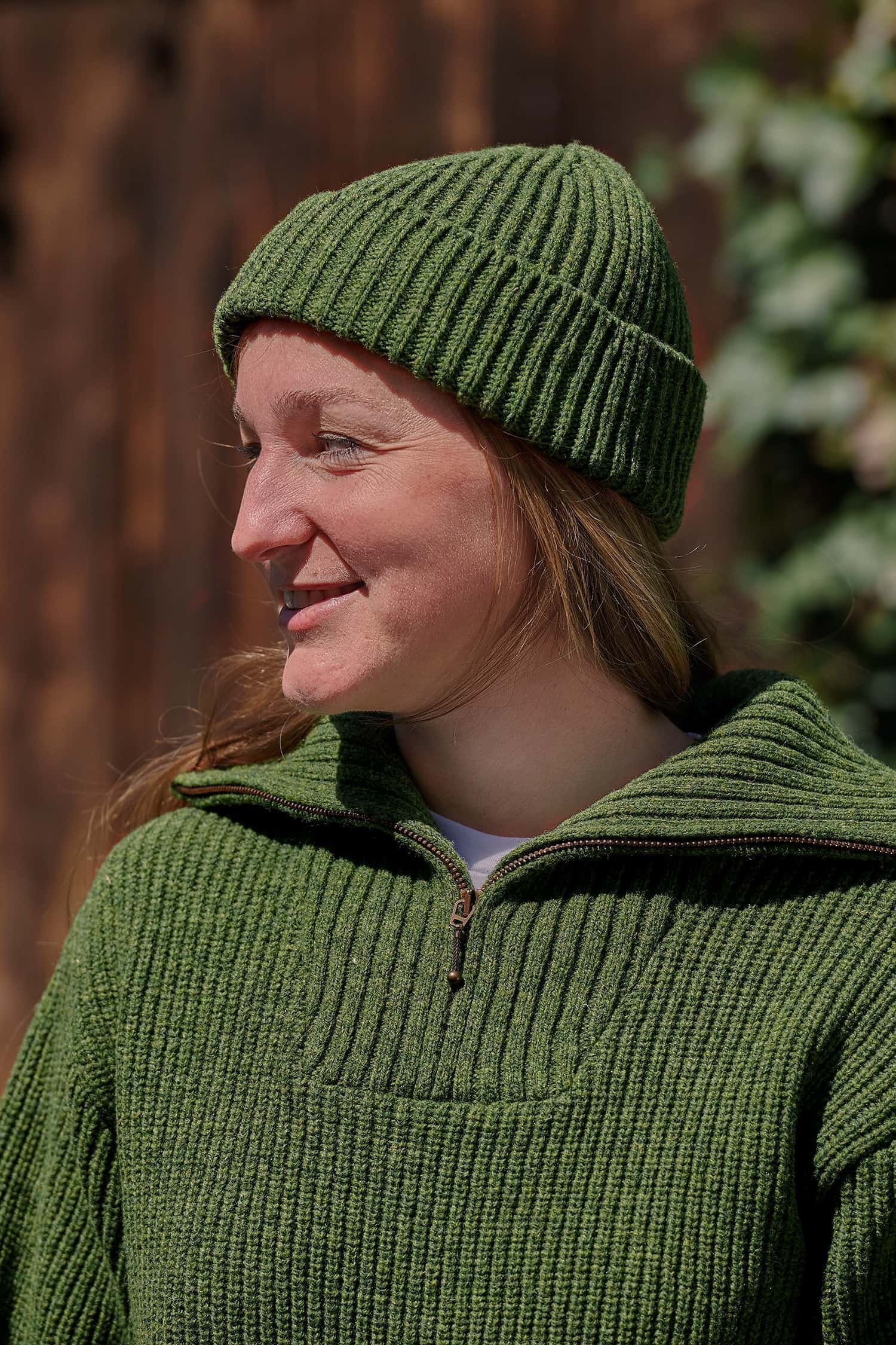 Frau trägt einen grünen Troyer und eine grüne Fischermütze aus Bio-Wolle vom Finkhof