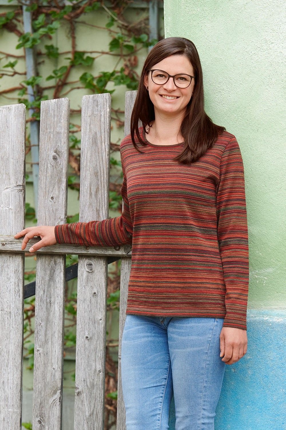 Frau mit grün rotem Ringelshirt aus bio Wolle (kbT) vom Finkhof steht vor einer grünen Hauswand