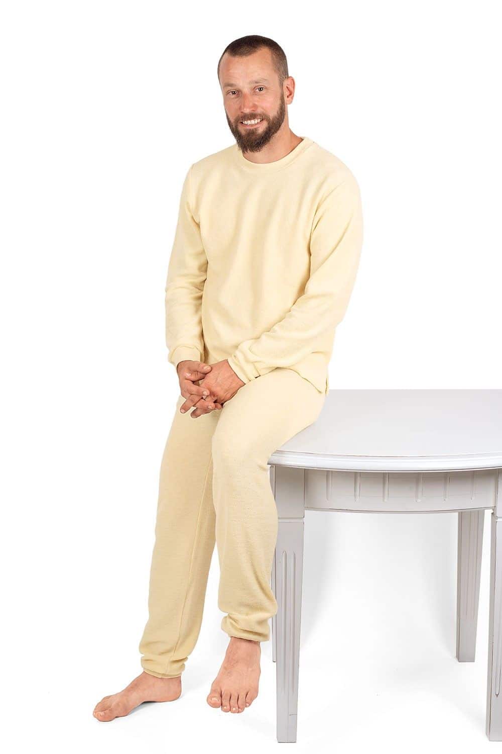 Mann sitzt auf Holztisch und trägt einen naturweißen Wollfrotte-Schlafanzüge aus bio Wolle (kbT)