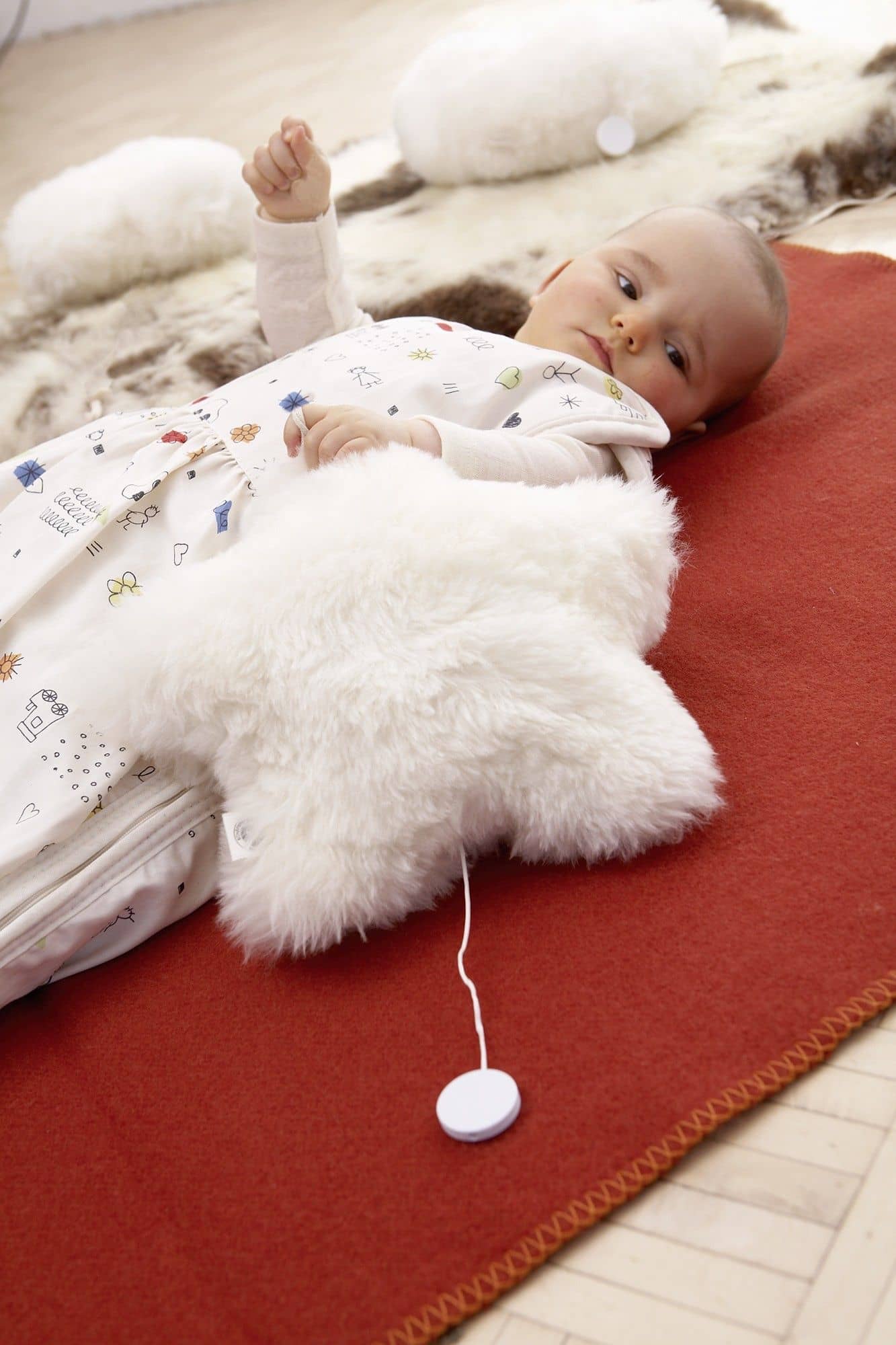 weiße Finkhof Spieluhr in Sternenform aus Fell und bio Wolle (kbT) auf rotem Untergrund neben liegendem Baby