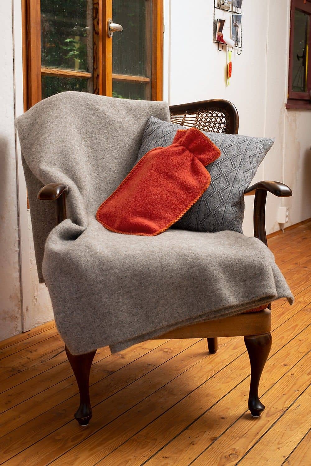 rostroter Wärmflaschenbezug aus bio Wolle (kbT) vom Finkhof mit grauem Kissen und Teppich auf einem Sessel