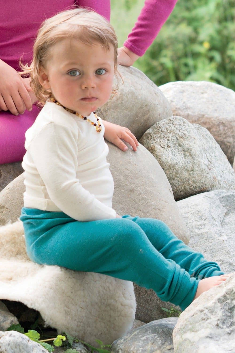 Kleinkind sitzt auf Steinen und trägt weißes Shirt und türkise lange Unterhose aus bio Wolle (kbT) und Seide
