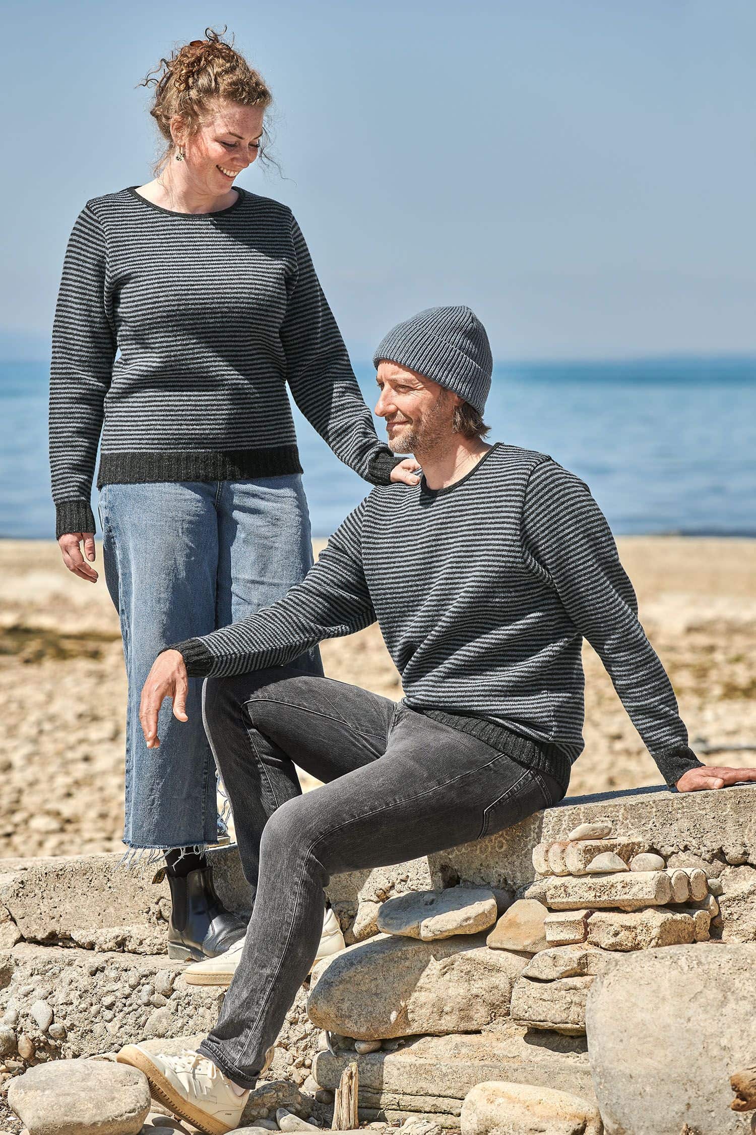 Finkhof-Streifenpullover rauchblau Gr. S Mann und Frau auf Steinen tragen Streifenpullis in rauchblau vom Finkhof aus bio Merinowolle (kbT)