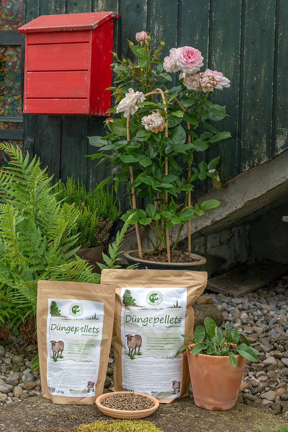 Düngepellets aus Schafschurwolle (kbT) Düngepellets aus Schafschurwolle in brauner Papierverpackung vor Holzfassade mit Blumen und Steinen