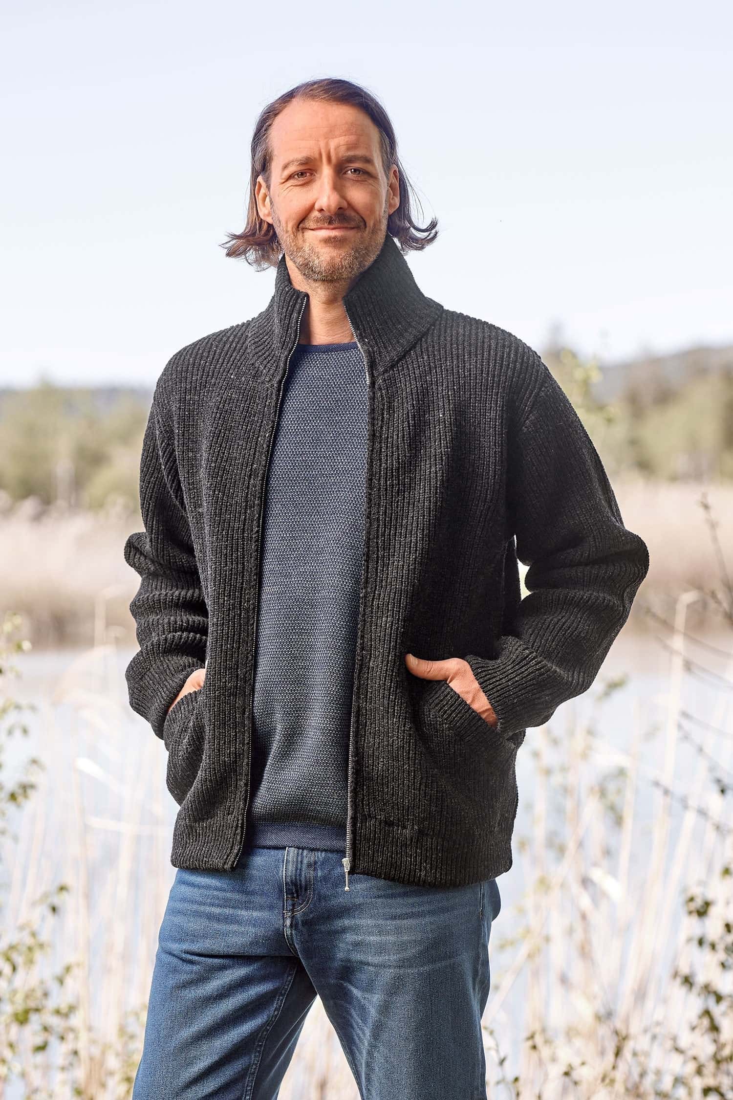 Mann mit blau meliertem Shirt trägt eine dunkelgraue Strickjacke mit Reißverschluss aus Bio-Wolle vom Finkhof