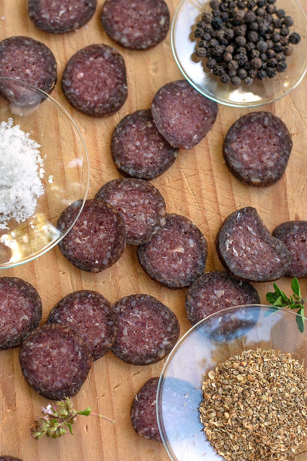 Stimmungsbild von in Scheiben geschnittener bio Finkhof Schafsalami auf einem Holzbrett mit Glasschälchen und Gewürzen