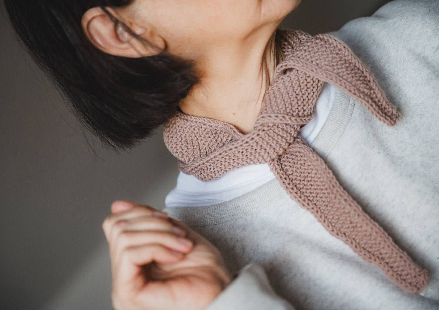 Frau mit kurzen Haaren und hellgrauem Pullover trägt altrosafarbenen Mini-Schal aus einer Wolle vom Finkhof