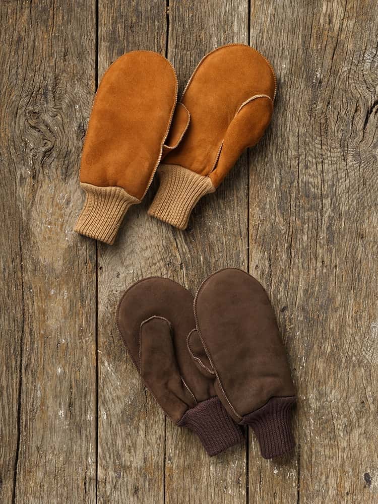 Fell-Fausthandschuhe mit Bund Fausthandschuhe aus Fell mit Bund in braun und hellbraun auf einem Holzboden