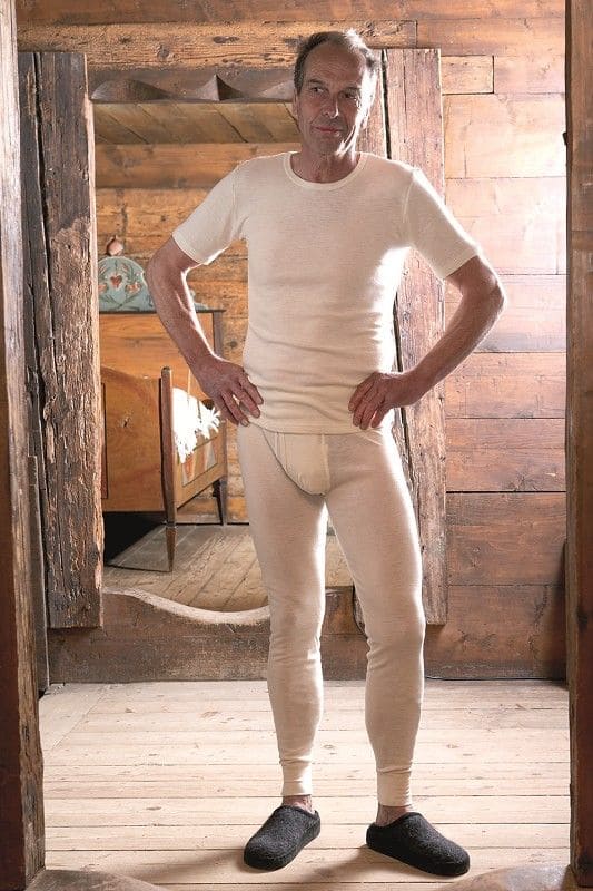Mann steht in Holztür und trägt naturweiße lange Wollunterhose aus bio Wolle (kbT) mit passendem Shirt