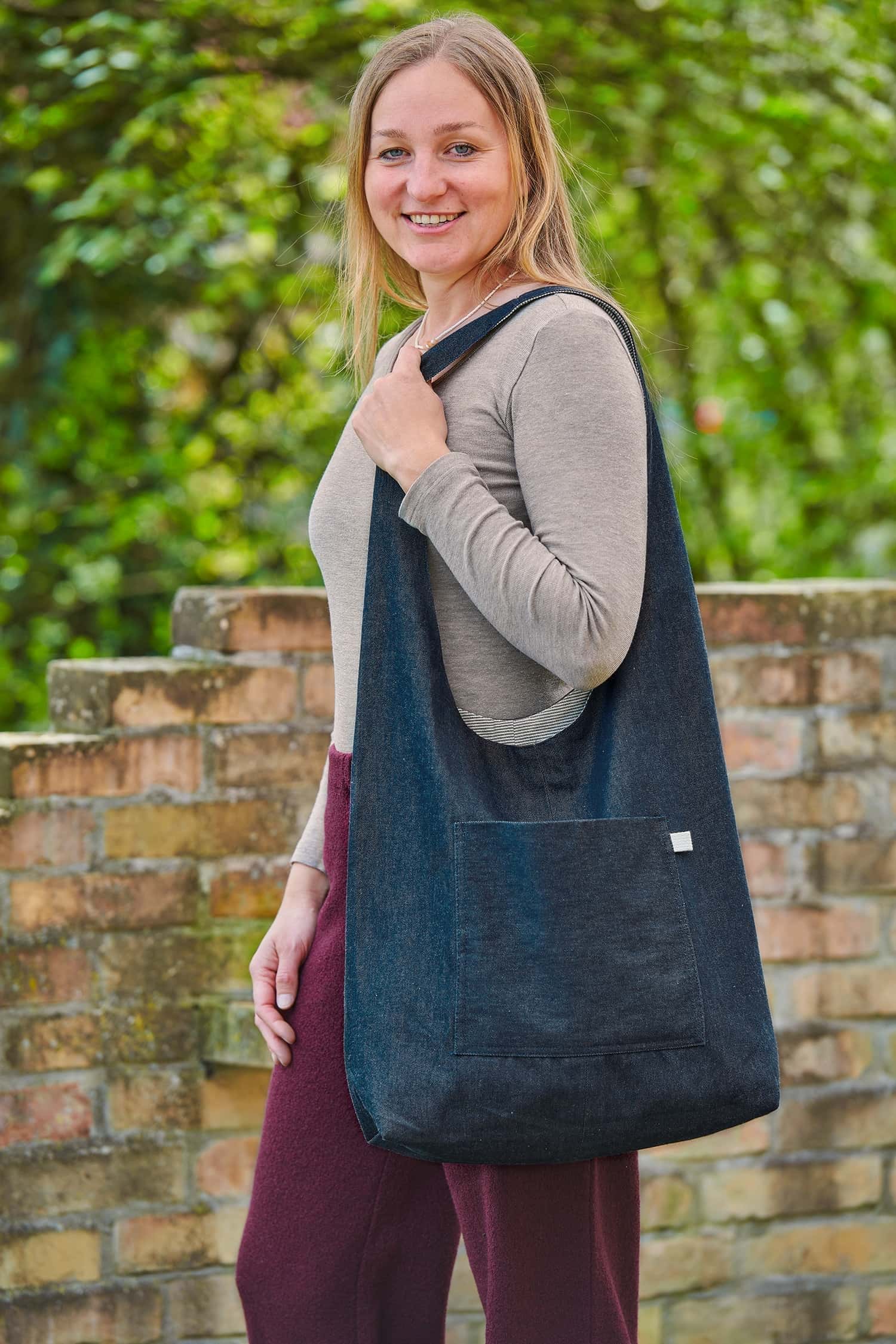 Frau mit Wollhose und Langarmshirt trägt eine große blaue Tasche aus Bio-Baumwolle zum Wenden vom Finkhof