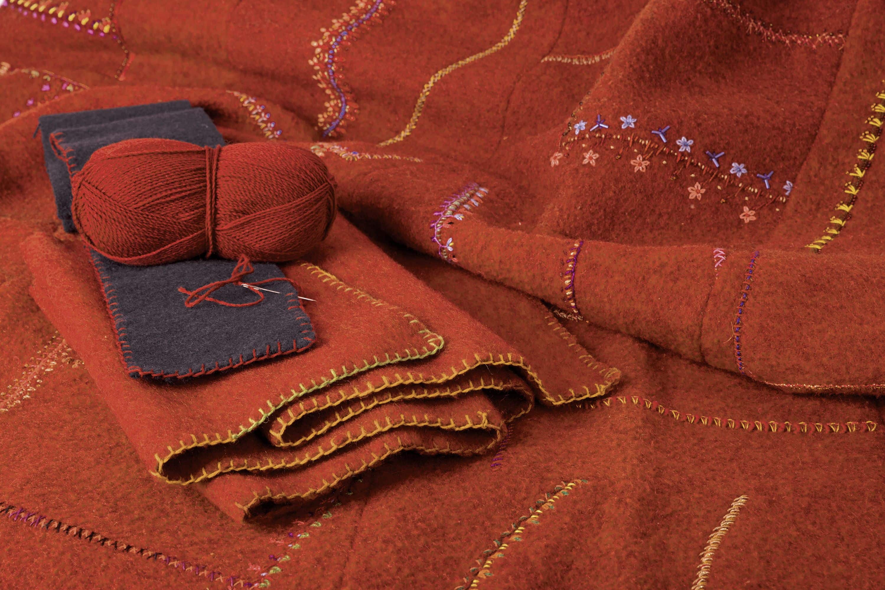orange Wolldecke mit Stickmuster und orangem Wollknäul, blauen Stoff darauf liegend
