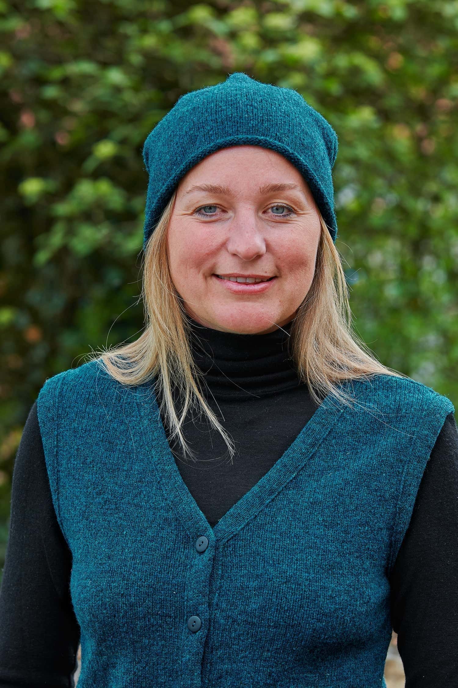 Frau trägt eine seeblaue Strickmütze mit Rollrand aus Bio-Wolle vom Finkhof mit passender Weste und einem schwarzen Shirt