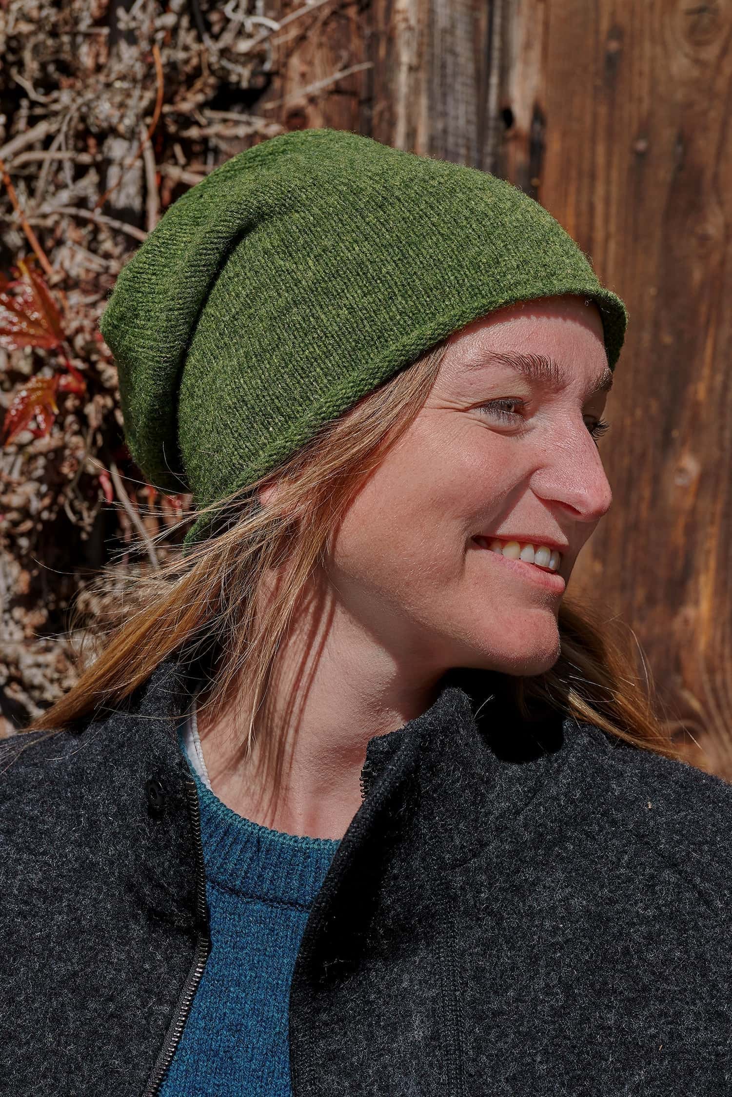 Frau trägt eine grüne Strickmütze vom Finkhof aus Bio-Wolle, einen türkisen Pulli und eine schwarze Jacke