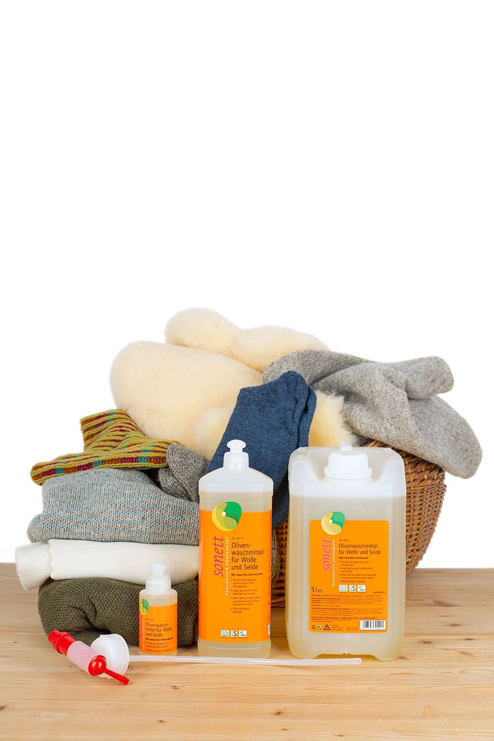 Olivenwaschmittel für Wolle und Seide mit Duft Olivenwaschmittel für Wolle und Seide in verschiedenen Verpackungseinheiten mit Wäsche im Korb im Hintergrund